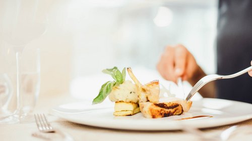 Willkommen im Hotel in Neustift im Stubaital! Person schneidet ein Gourmetgericht mit Kartoffelpüree und Basilikum auf weißem Teller