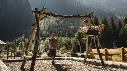 Willkommen im Hotel in Neustift im Stubaital! Junge schaukelt, während Erwachsener ihn auf einem Spielplatz in den Bergen anschubst