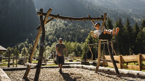 Willkommen im Hotel in Neustift im Stubaital! Junge schaukelt, während Erwachsener ihn auf einem Spielplatz in den Bergen anschubst