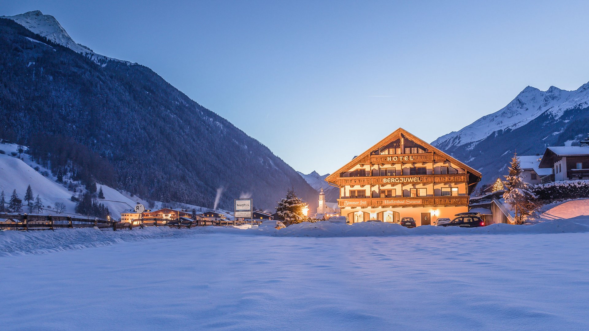 Willkommen im Hotel in Neustift im Stubaital! Beleuchtetes Hotel in verschneiter Berglandschaft bei Dämmerung