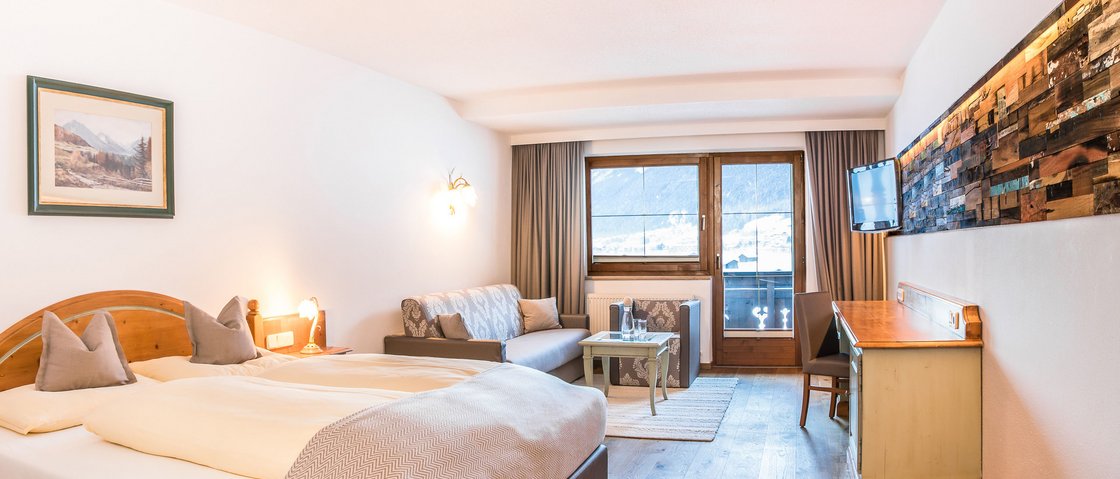 Willkommen im Hotel in Neustift im Stubaital! Hell eingerichtetes Hotelzimmer mit Doppelbett, Sofa, Schreibtisch und Bergblick