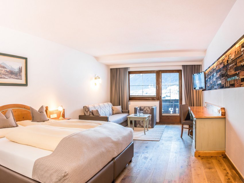 Willkommen im Hotel in Neustift im Stubaital! Hell eingerichtetes Hotelzimmer mit Doppelbett, Sofa, Schreibtisch und Bergblick