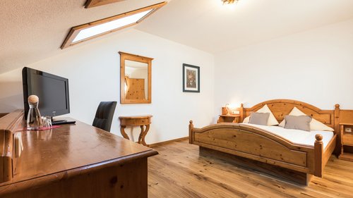 Willkommen im Hotel in Neustift im Stubaital! Gemütliches Hotelzimmer mit Holzmöbeln, Doppelbett und Schreibtisch unter Dachschräge