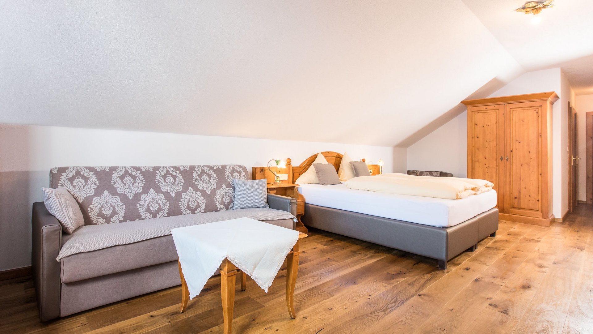 Willkommen im Hotel in Neustift im Stubaital! Gemütliches Gästezimmer mit Bett, Sofa und Holzschrank unter Dachschräge